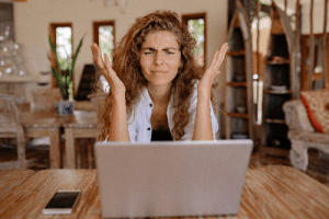 frustrated woman sitting in front of laptop while throwing her hands up